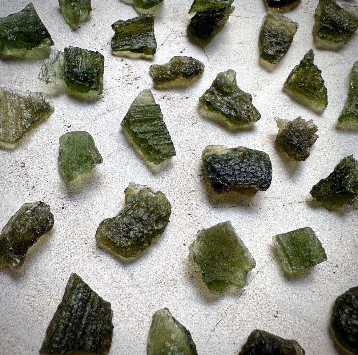 Authentic Moldavite crystals scattered on a surface, showcasing unique green hues and textures.