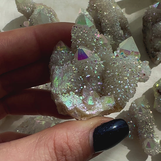 Hand holding a sparkling Angel Aura Spirit Quartz crystal with iridescent colors on a soft surface.