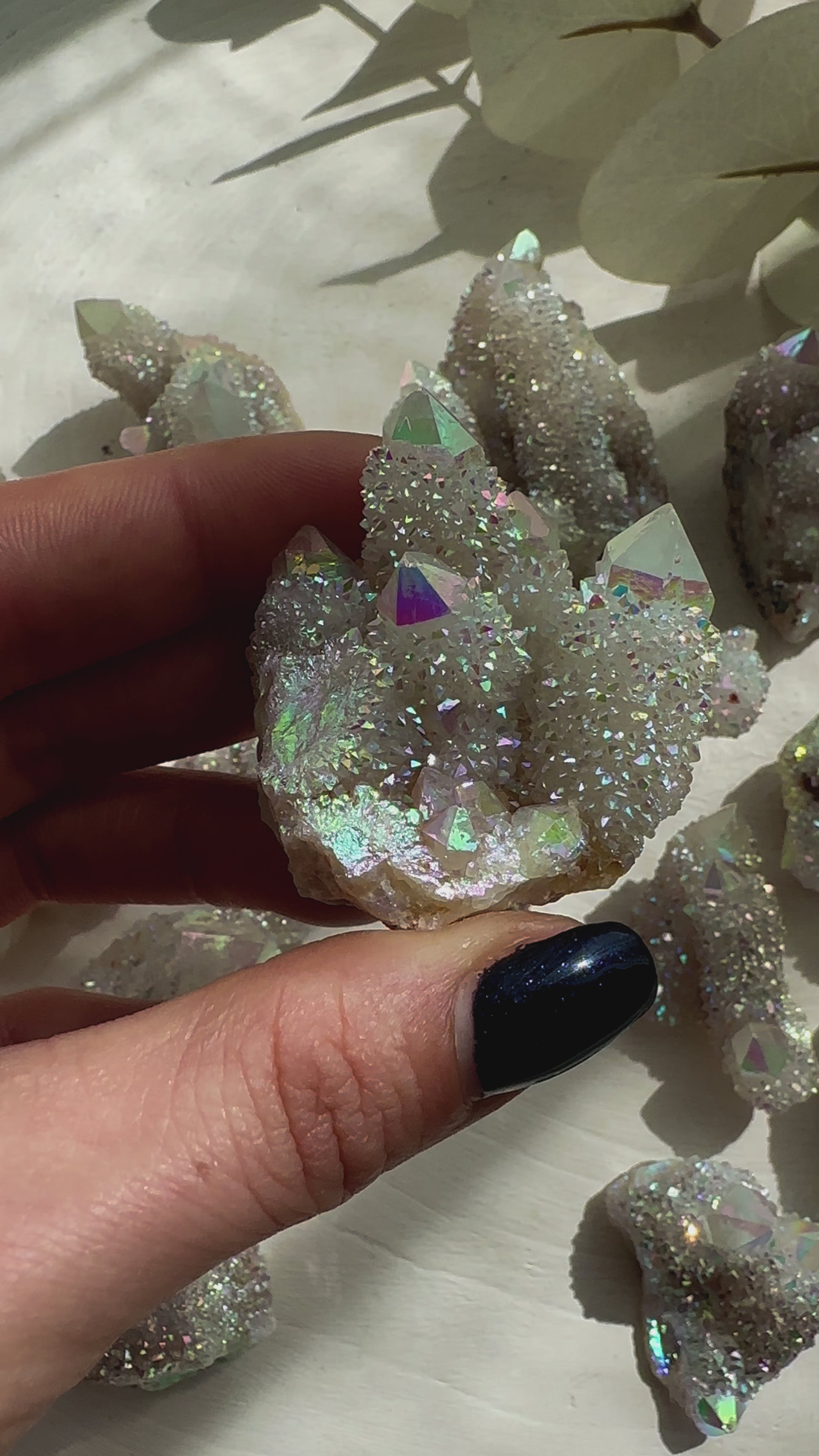Hand holding a sparkling Angel Aura Spirit Quartz crystal with iridescent colors on a soft surface.